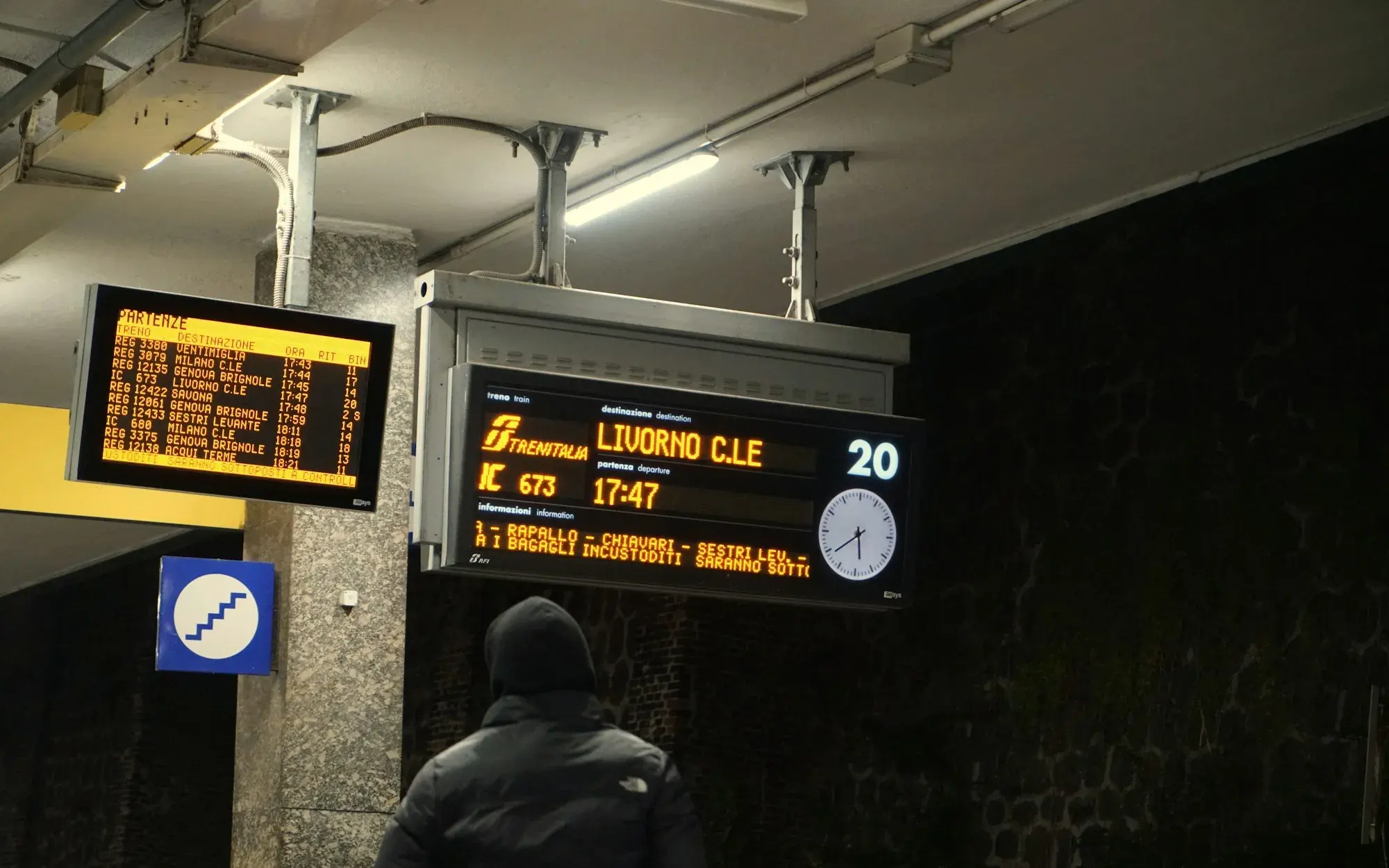 Digital departure screens hanging above a platform at Pisa station