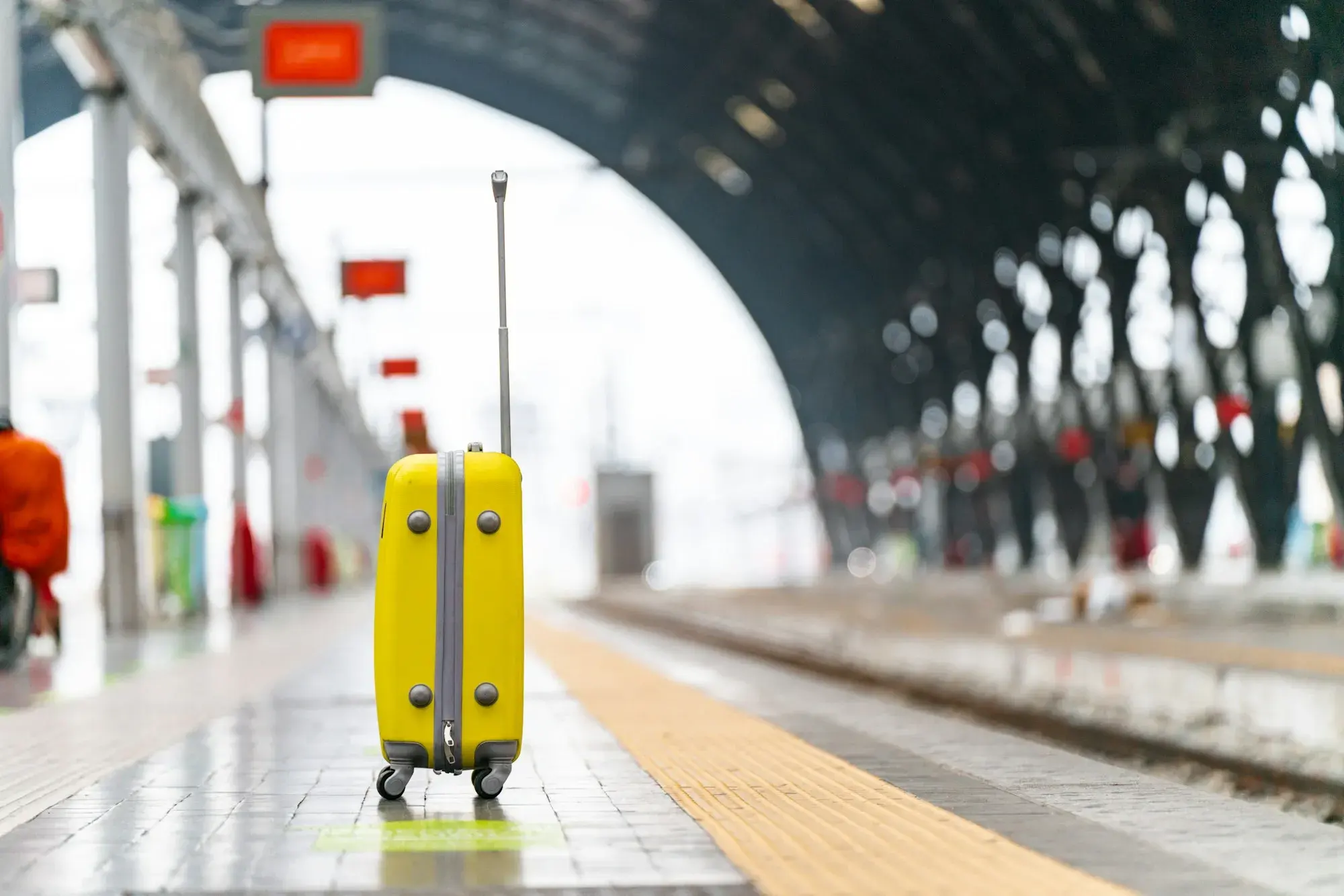 A yellow suitcase standing on an empty platform at Milano Centrale