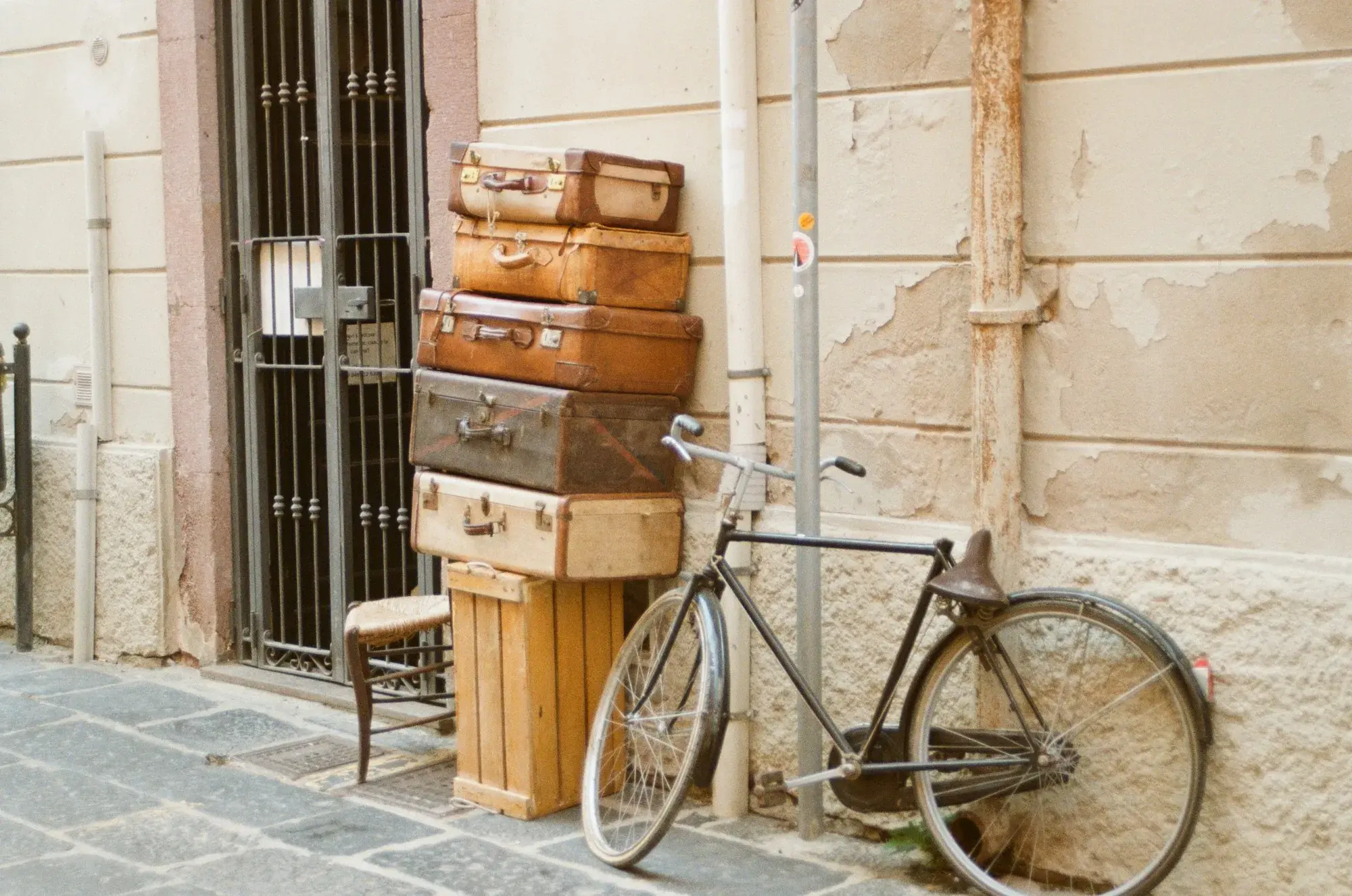 A stack of vintage suitcases and a bicycle outside a building on a stone-paved street in Bosa, Sardinia