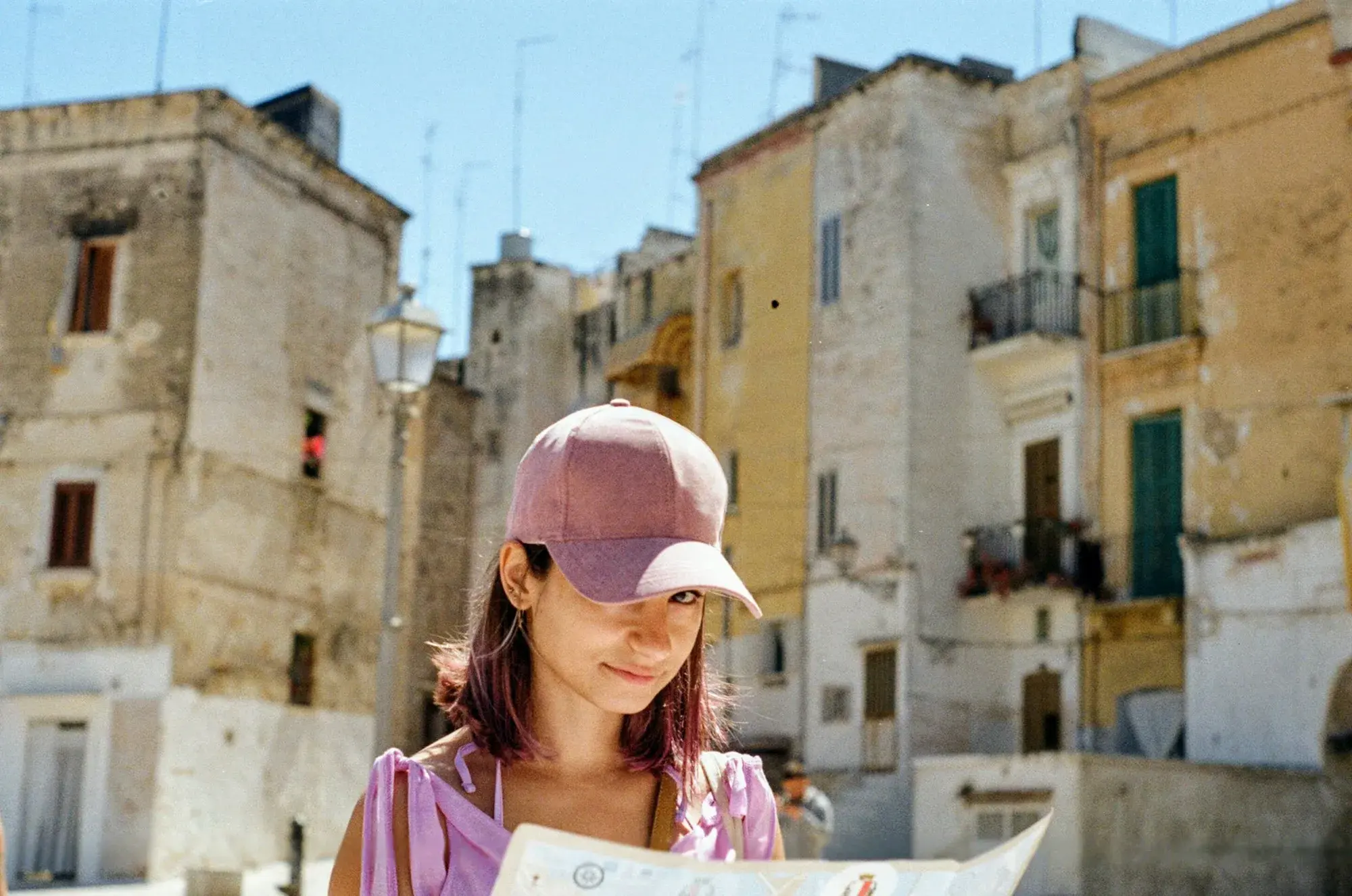 A young woman in a pink cap studying a map on a street in the old town of Bari