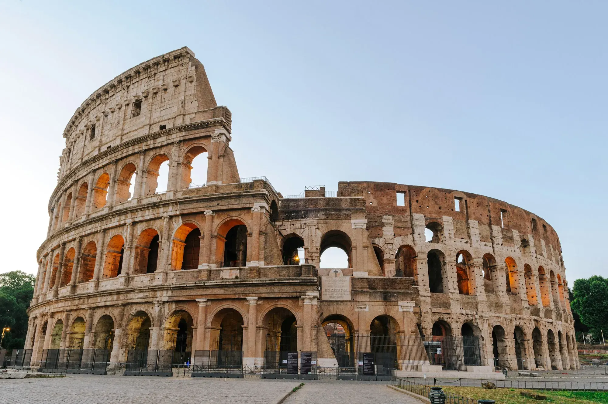 The Colosseum in Rome in early morning light, its arched outer wall glowing golden under a pale sky