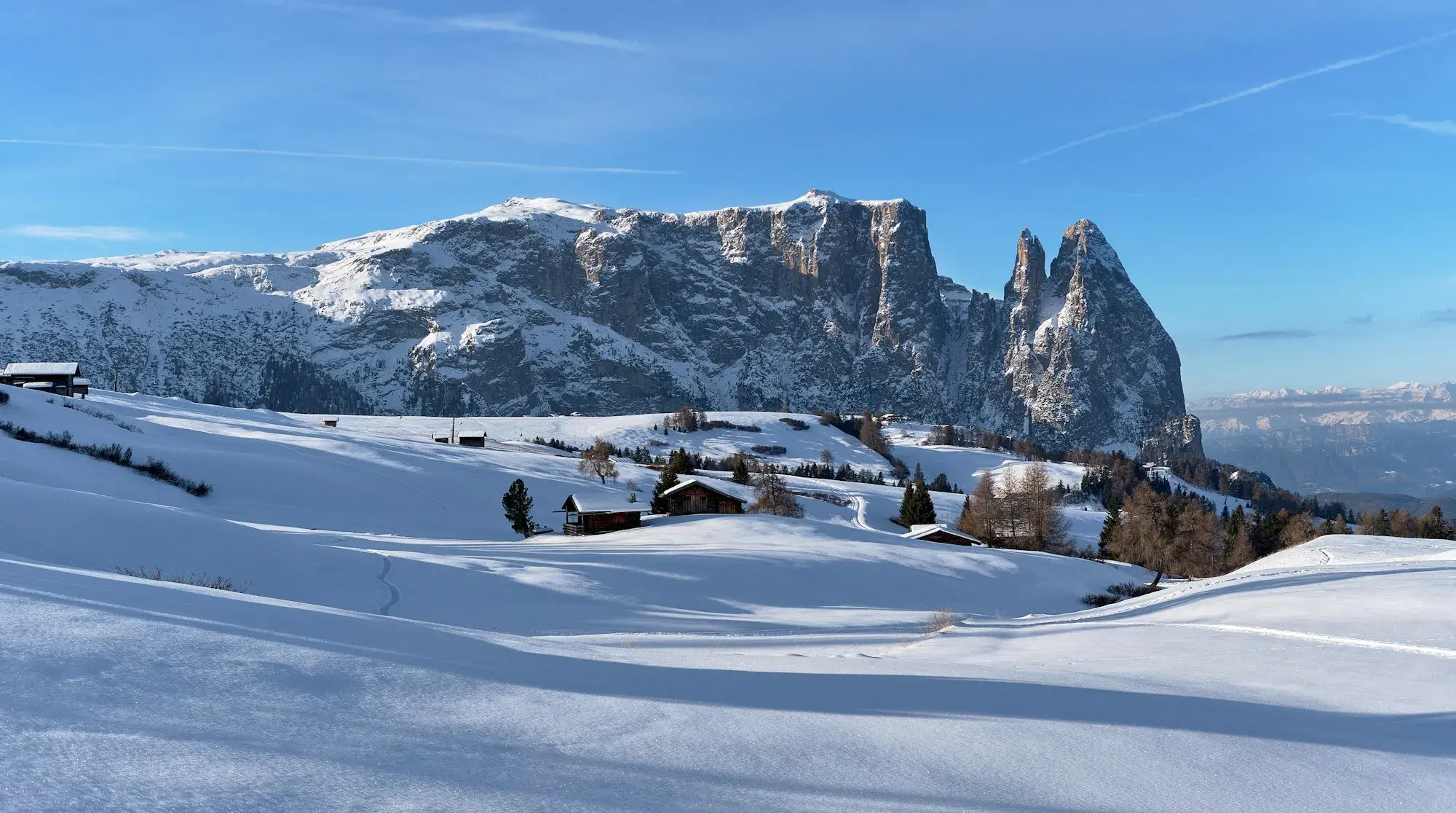 Snow-covered pastures and wooden huts on the Alpe di Siusi, below the Sciliar massif in winter