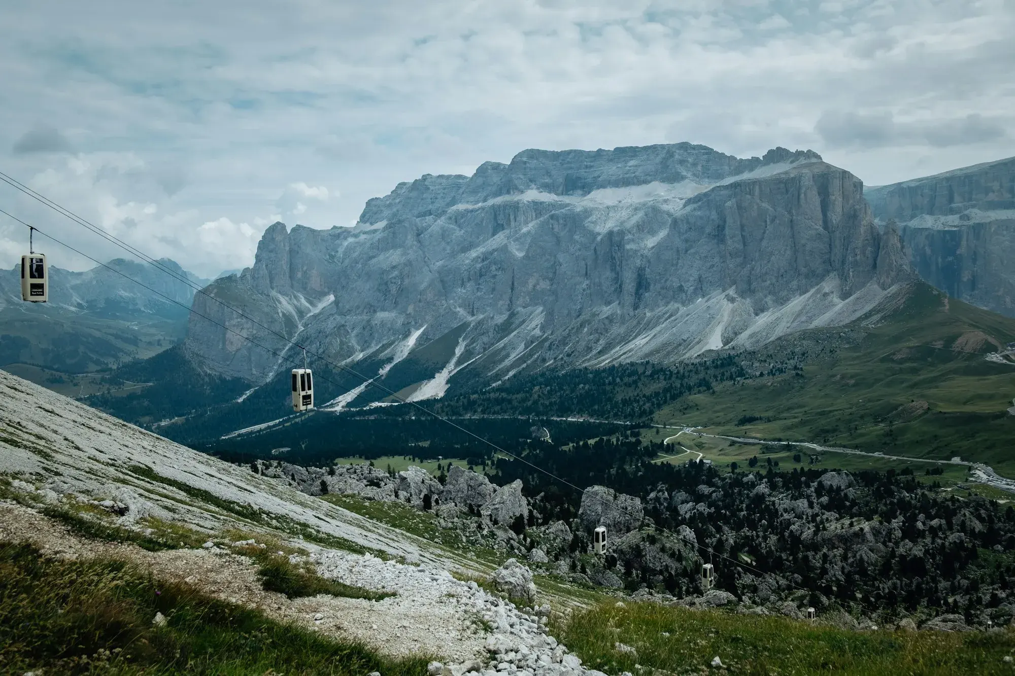 Cable car cabins crossing a valley towards a massive grey rock wall above Campitello di Fassa