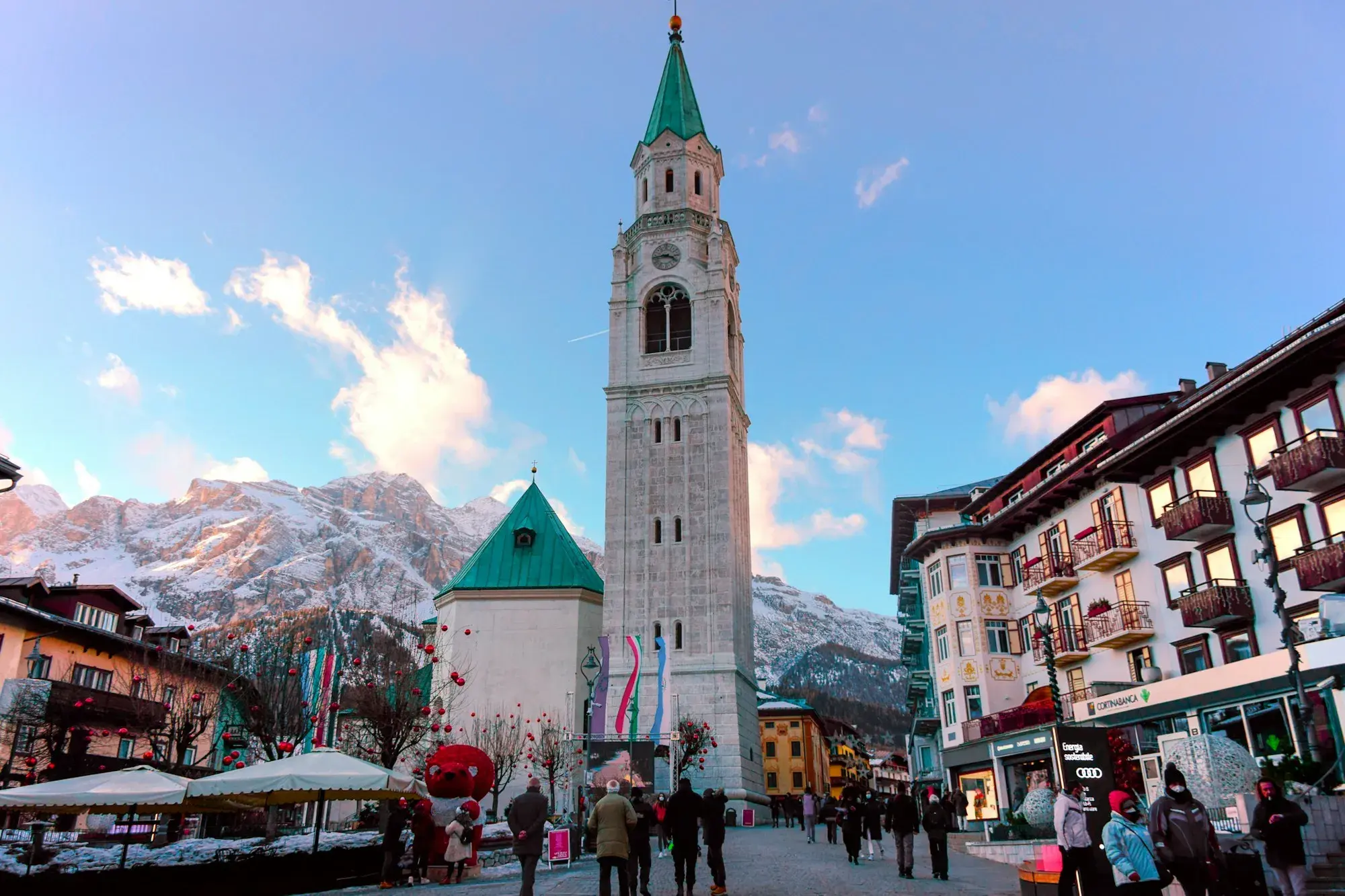 The tall bell tower and church in the centre of Cortina d'Ampezzo, with hotels, people walking and mountains behind