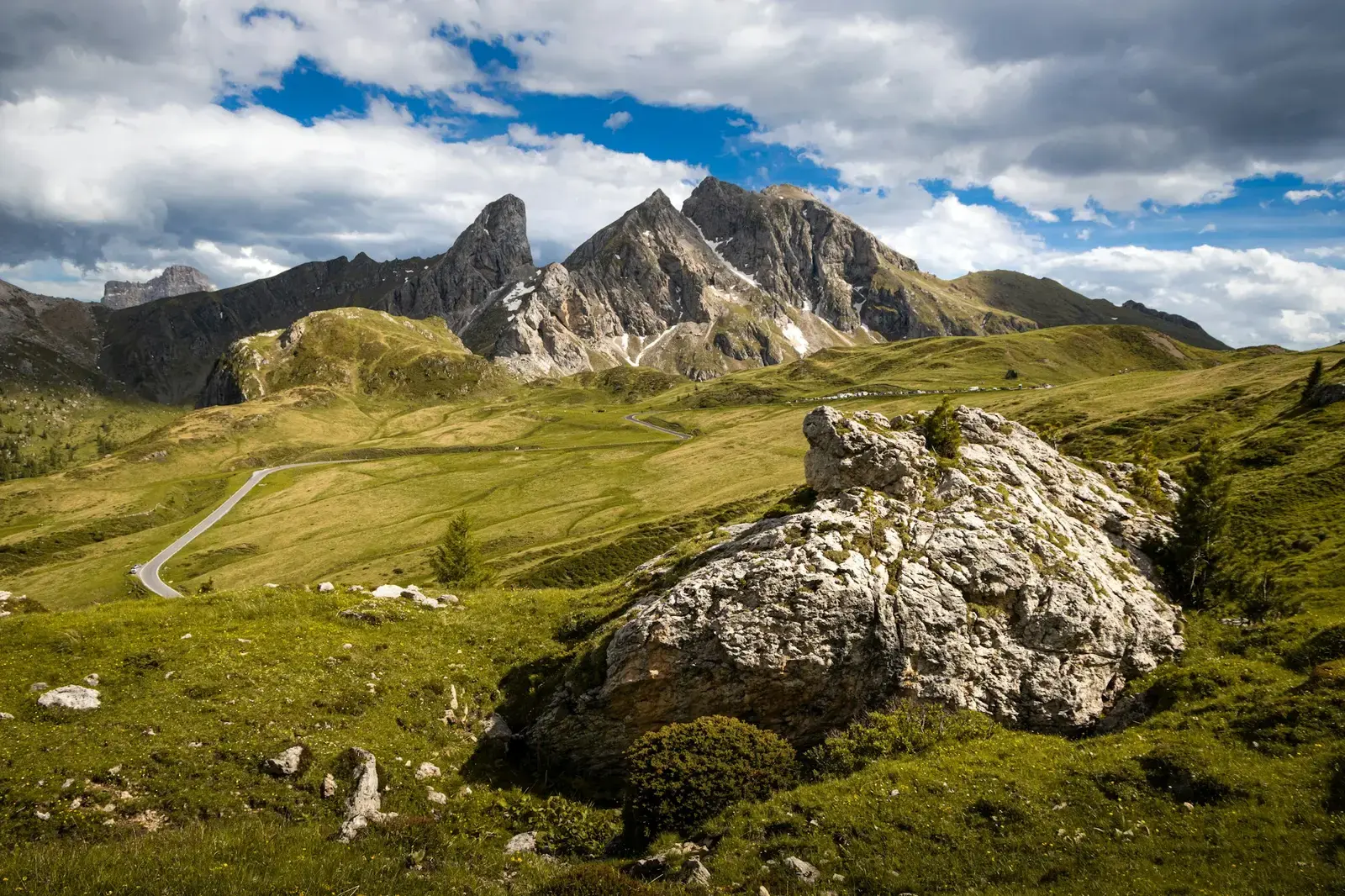 A mountain road winding across green slopes and rocks below jagged peaks near Passo Giau