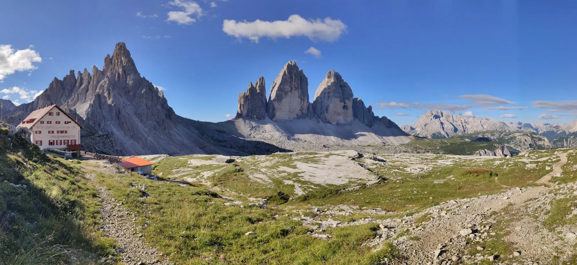 The three rock towers of the Tre Cime di Lavaredo rising above a rocky plateau, with a mountain hut on the left