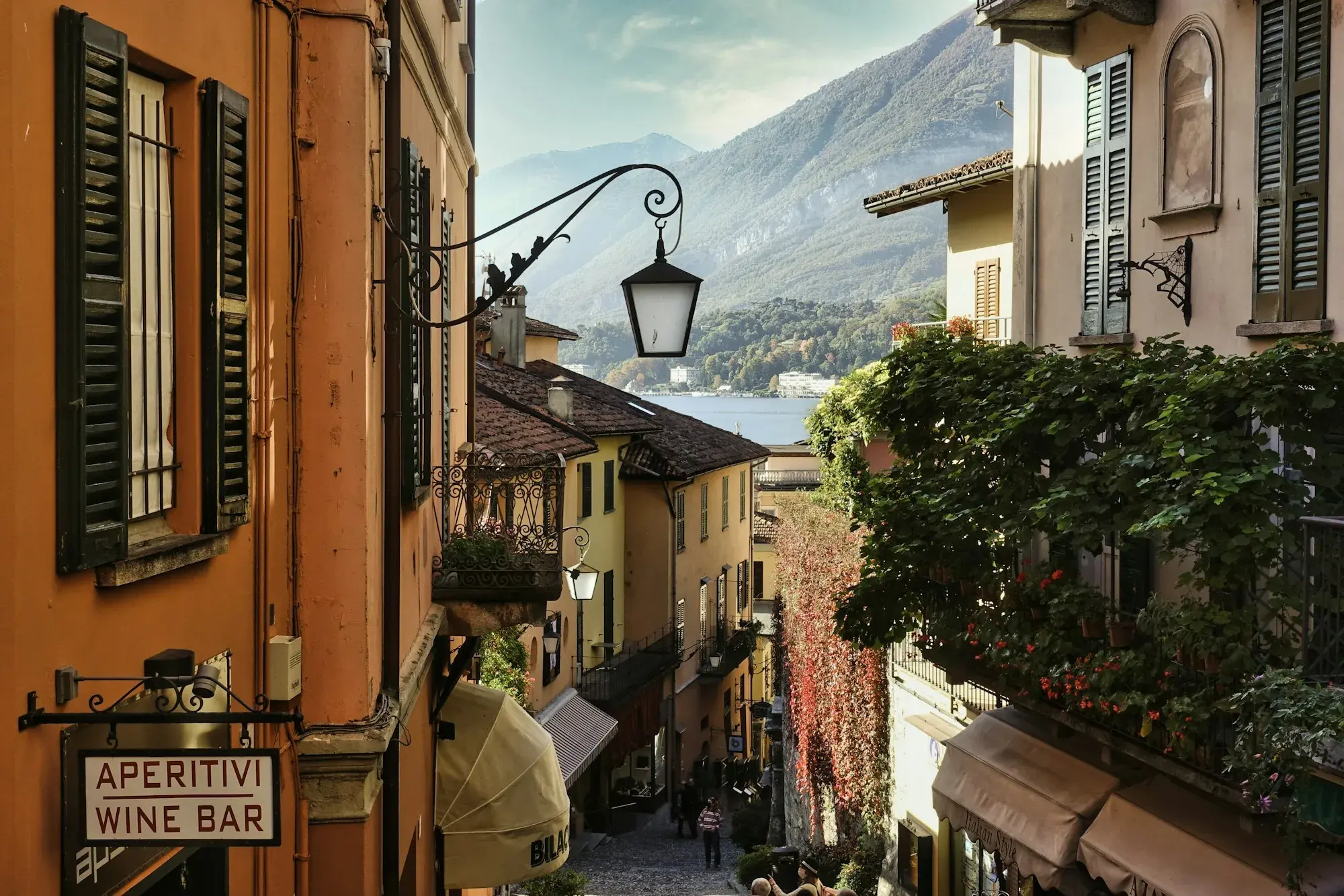A narrow lane in Bellagio with tables outside a wine bar and the lake and mountains beyond
