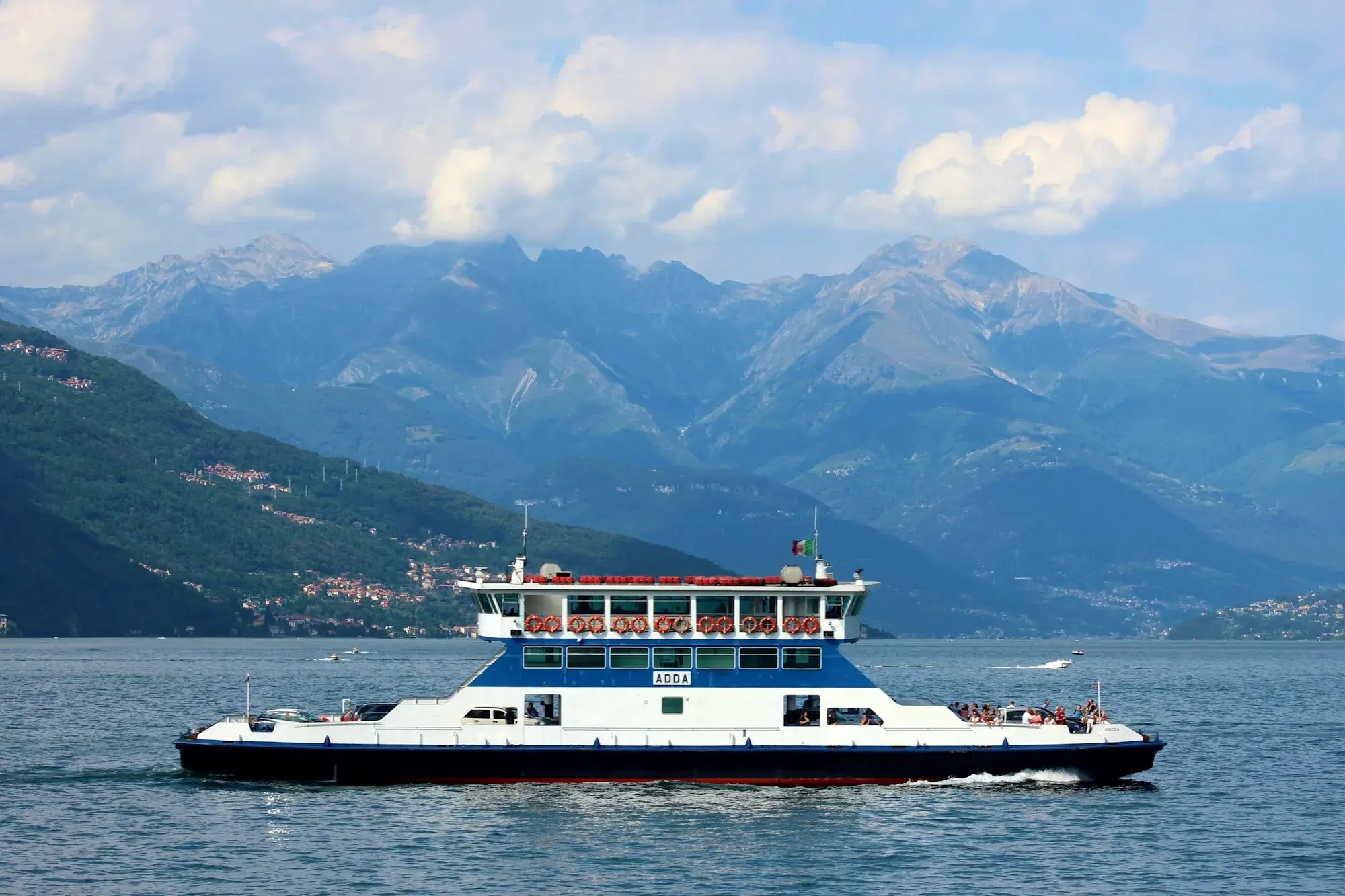 A white passenger and car ferry crossing Lake Como with mountains behind