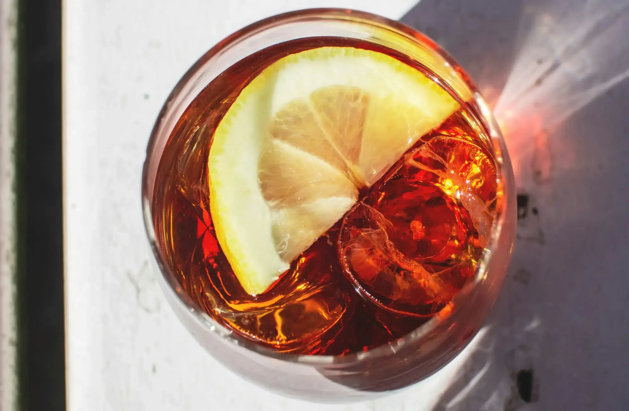 Un aperitivo rosso con ghiaccio e una fetta di limone in un tumbler, visto dall'alto