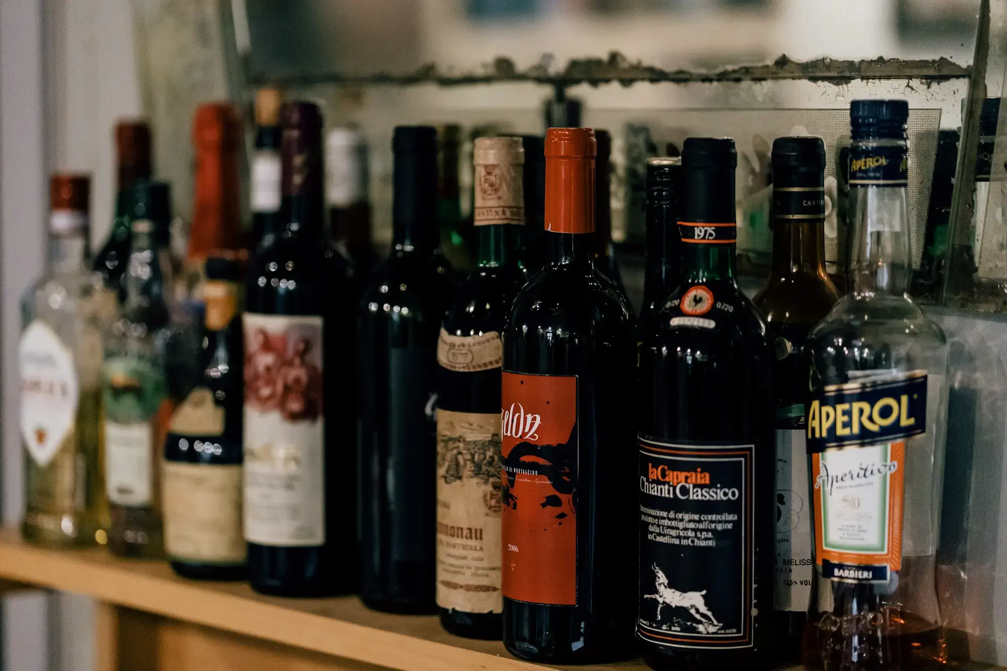 Bottiglie di vino, bitter e liquori italiani, tra cui un bitter da aperitivo, allineate su uno scaffale di legno in una trattoria di Roma