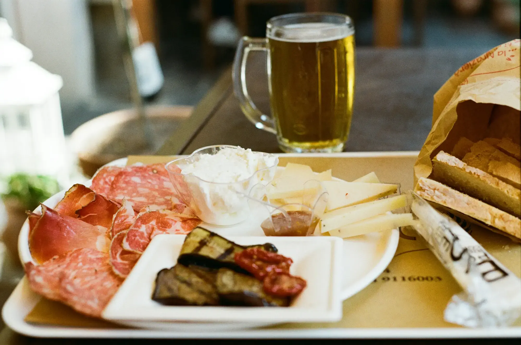 Un vassoio di salumi, formaggio, melanzane grigliate e pane con un bicchiere di birra sul tavolino di un bar in Toscana