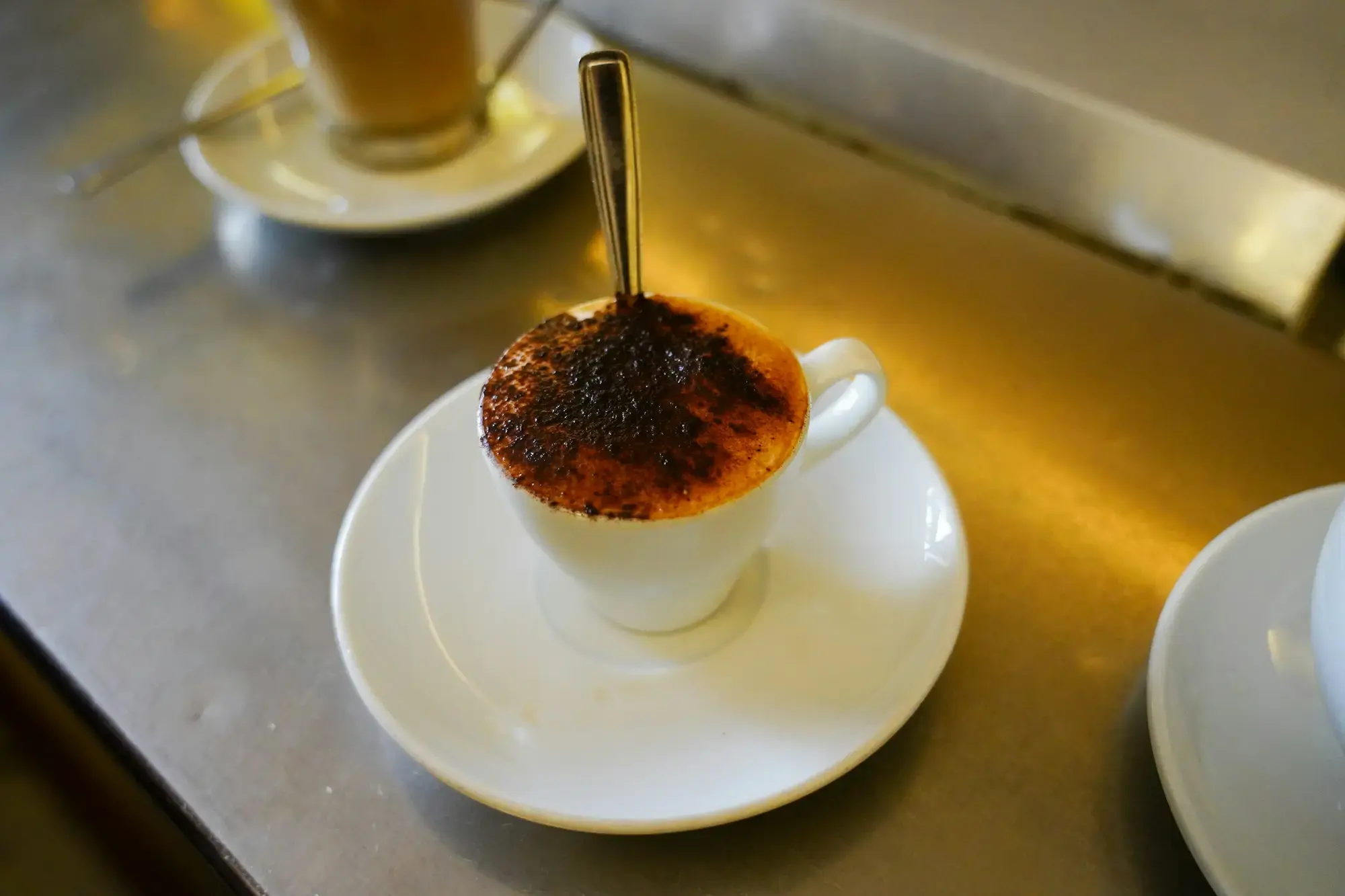 A cappuccino in a white ceramic cup on a saucer at a café table