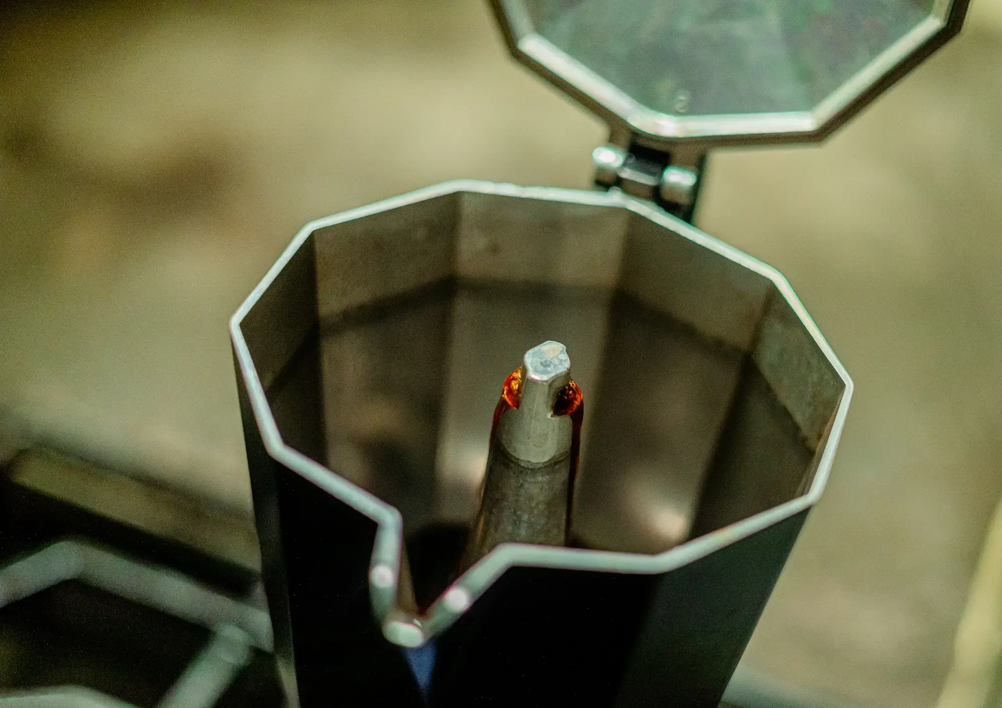 A moka pot on a hob with dark coffee rising through the central column into the upper chamber