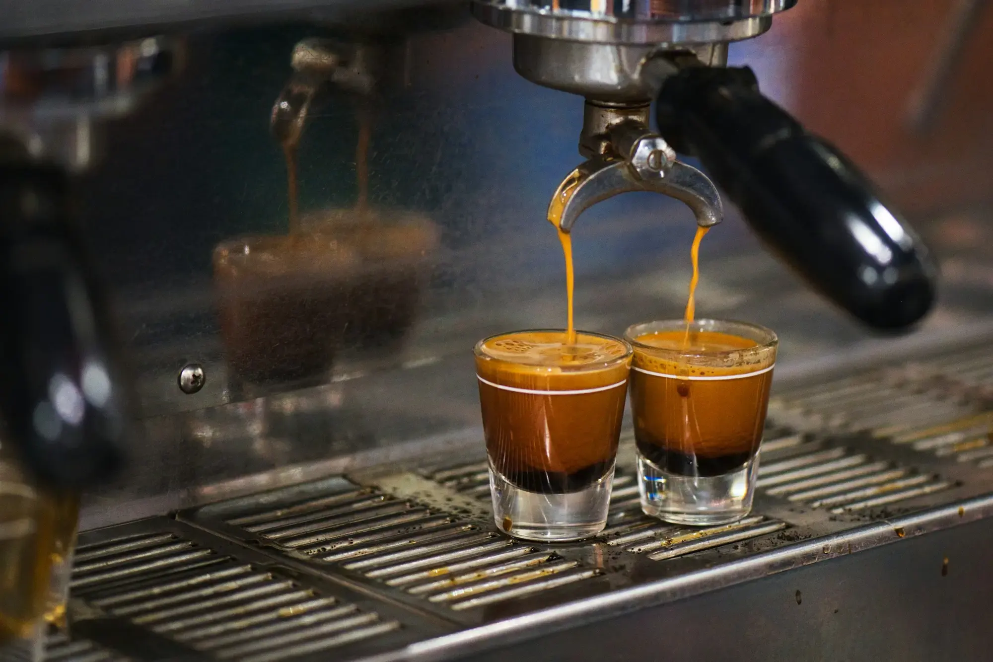 Two small white espresso cups resting on a chrome espresso machine at an Italian bar counter