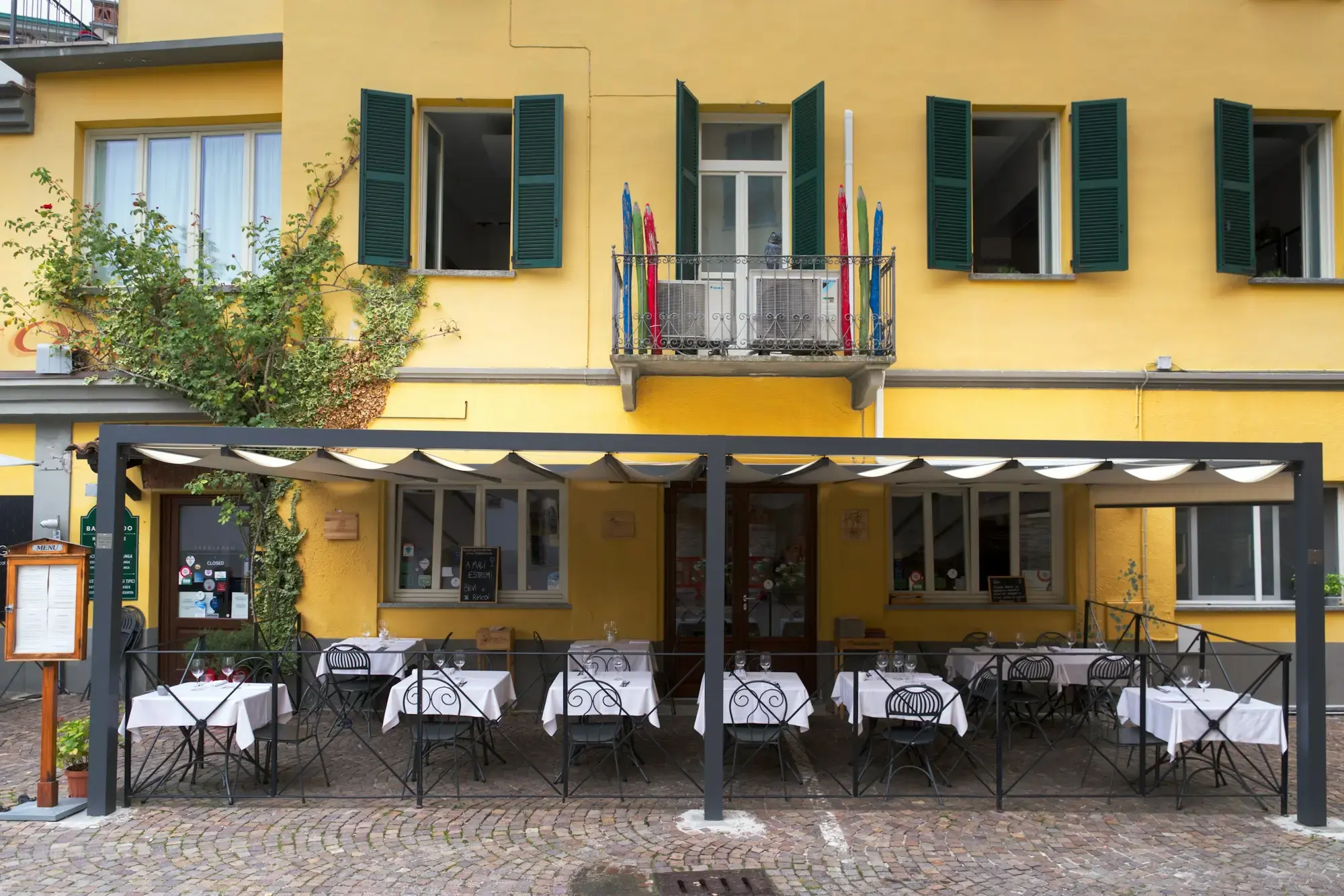Empty outdoor restaurant tables set with glasses and napkins, ready for dinner service in an Italian piazza