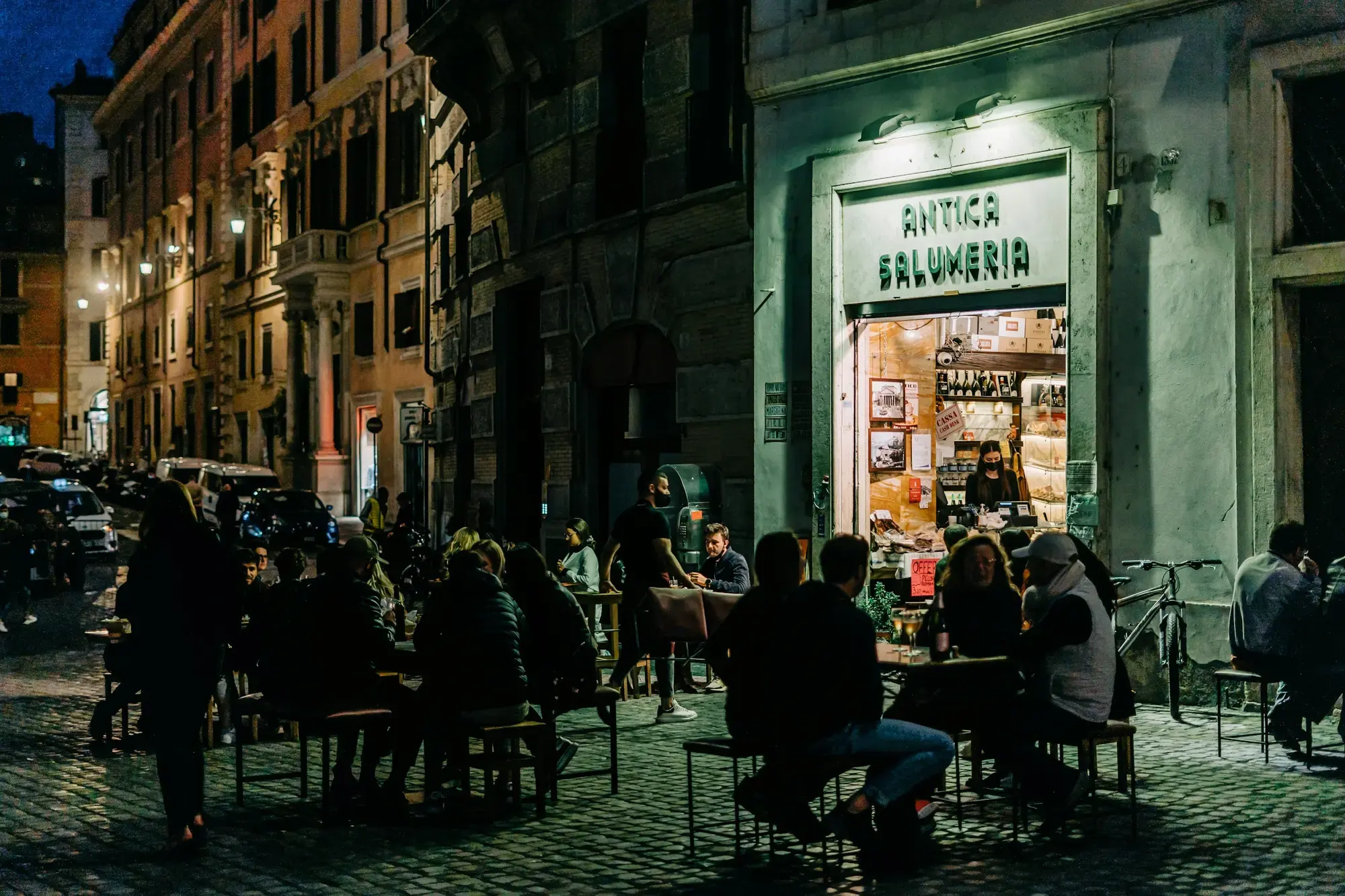 A group of people dining at outdoor tables at an Italian restaurant on a sunny day