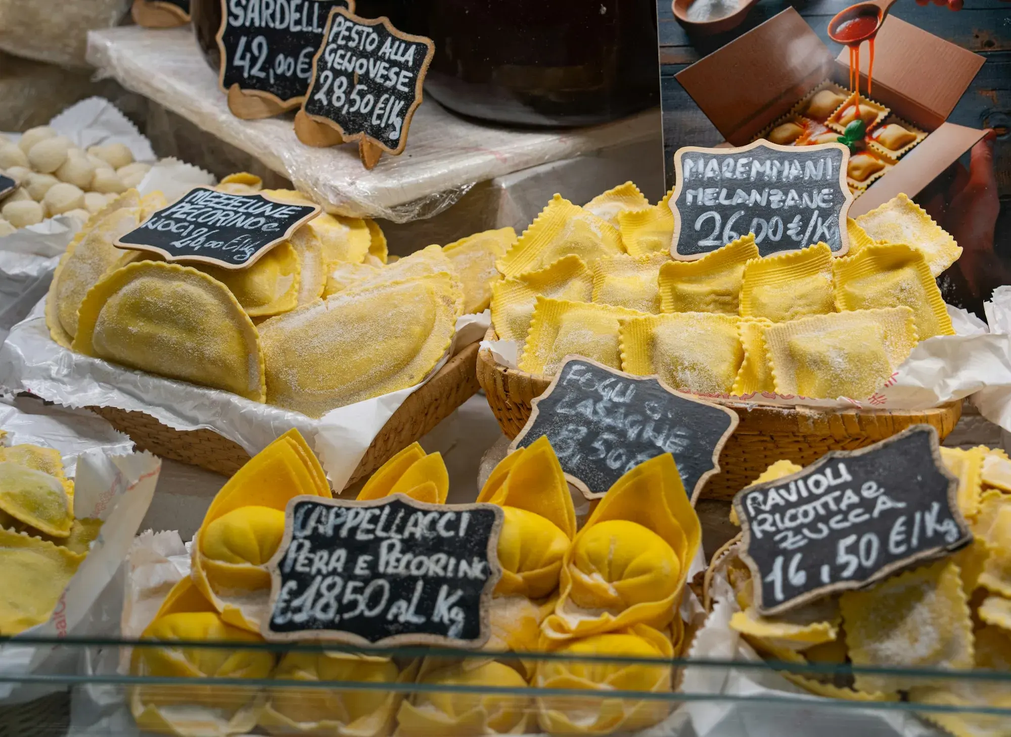 Trays of fresh filled pasta — cappellacci and ravioli — with handwritten price labels at a market in Florence