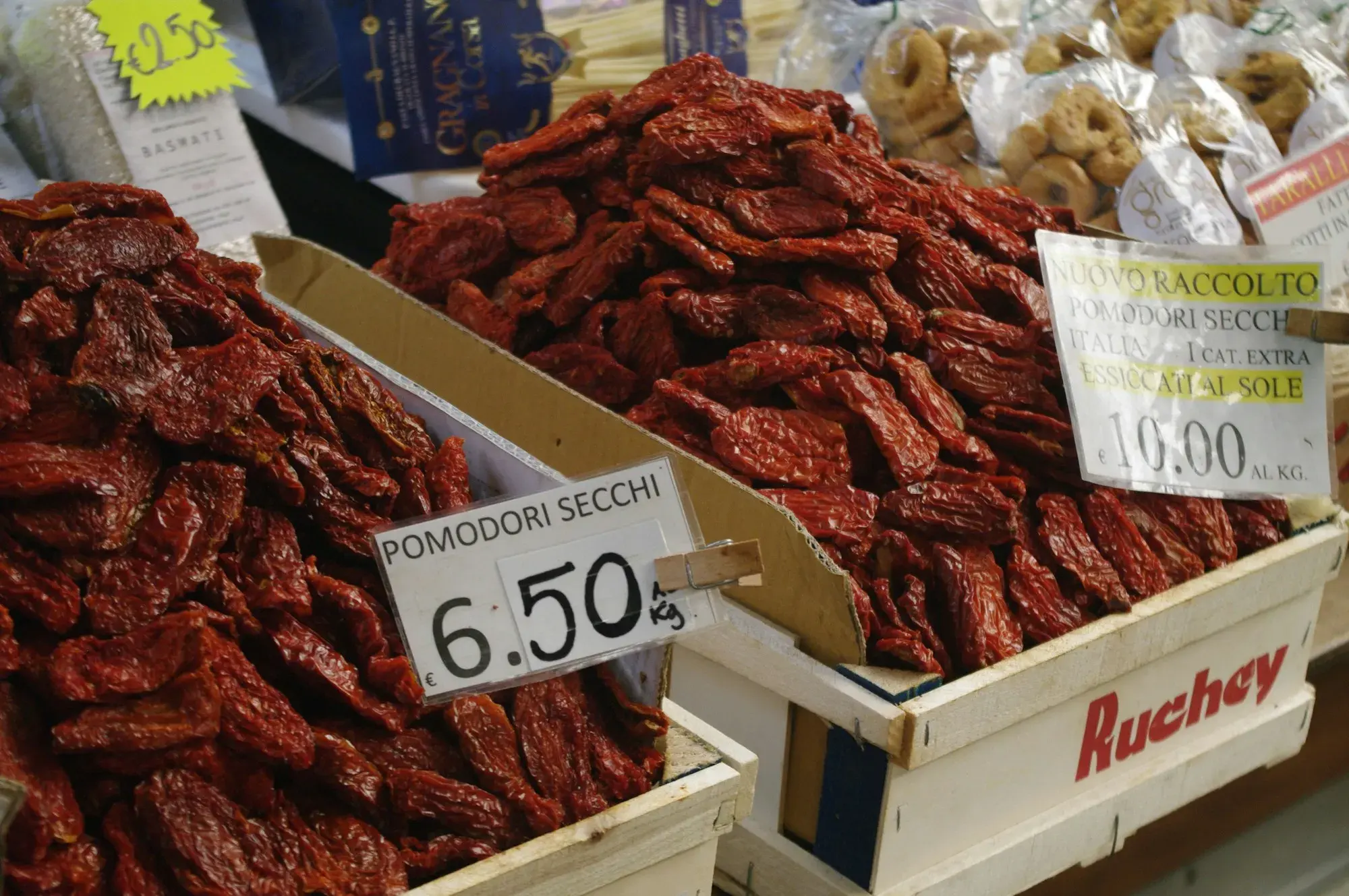 Crates of dark red sun-dried tomatoes with price labels at a market stall in Genoa