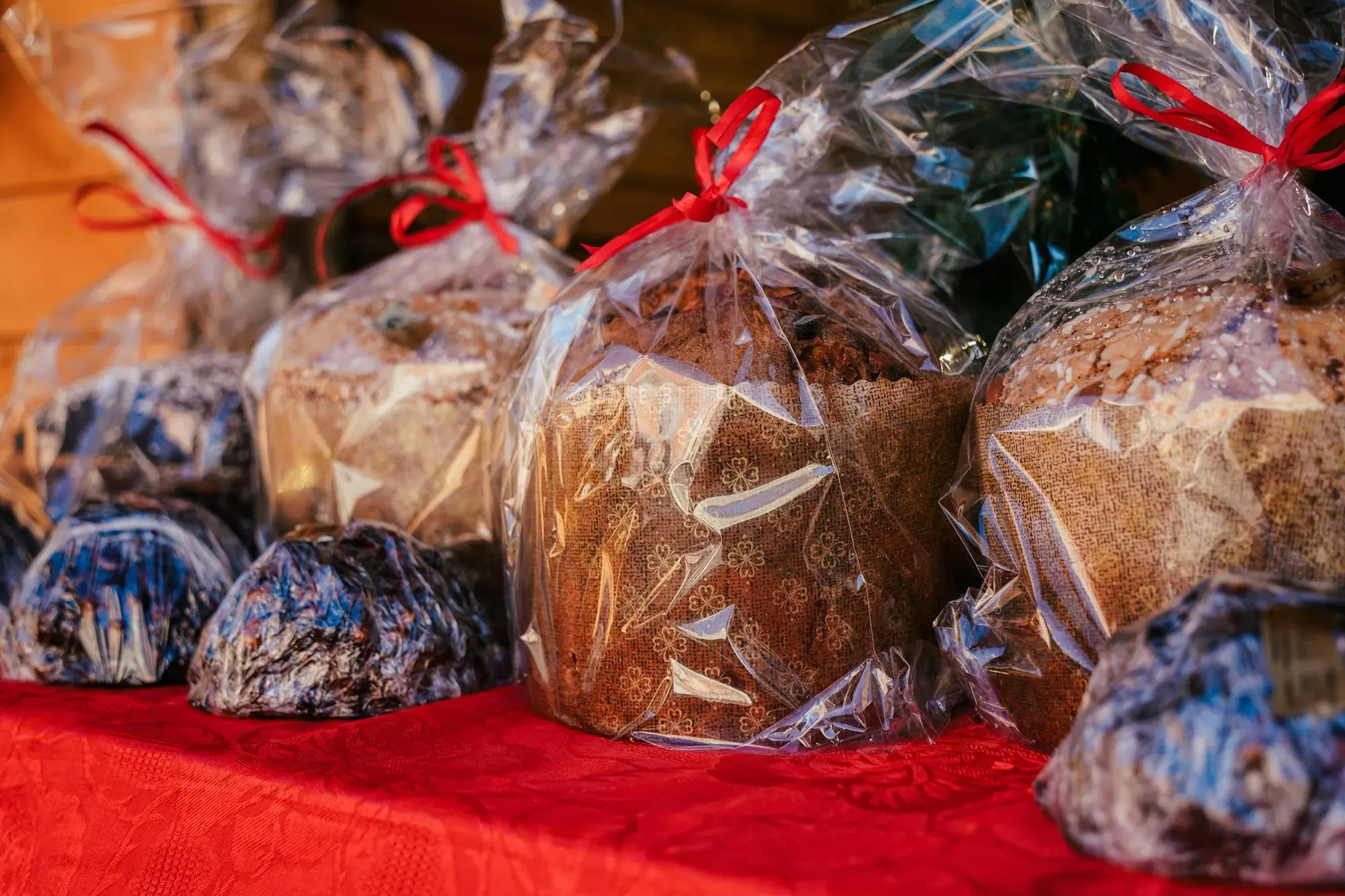 Panettoni wrapped in clear cellophane with red ribbons on a stall covered with a red cloth