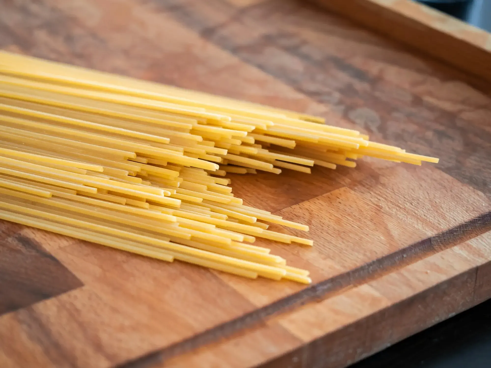 Un tagliere di legno coperto di pasta fresca in vari formati e dimensioni, pronta per la cottura