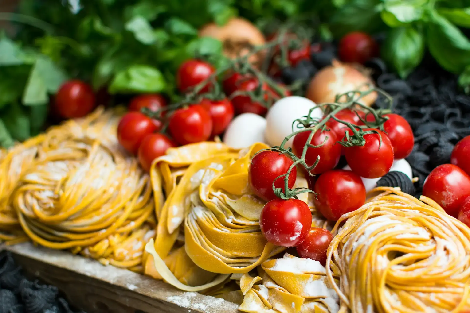 Un nido di tagliatelle non cotte con pomodori ciliegia su una superficie scura, che mostra i nastri dorati della pasta all'uovo