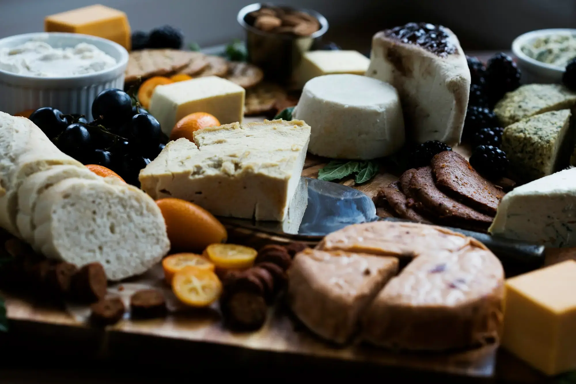 A wooden board with a range of Italian cheeses of different textures, colours and ages, with crackers and small accompaniments