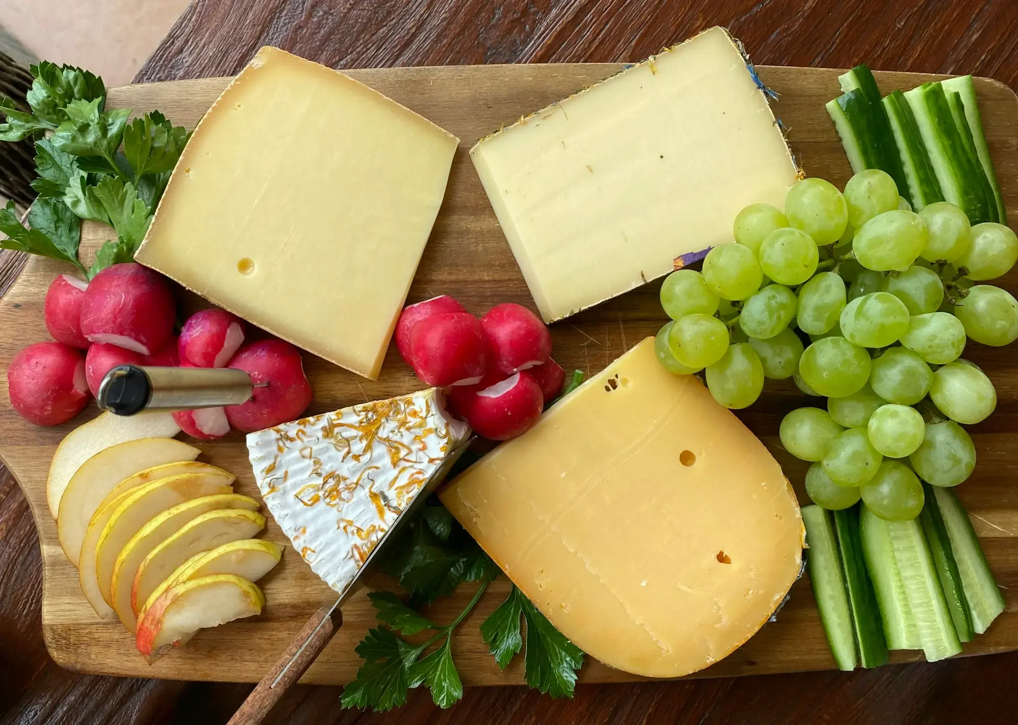 A wooden cutting board loaded with a selection of different cheeses, fruit and accompaniments