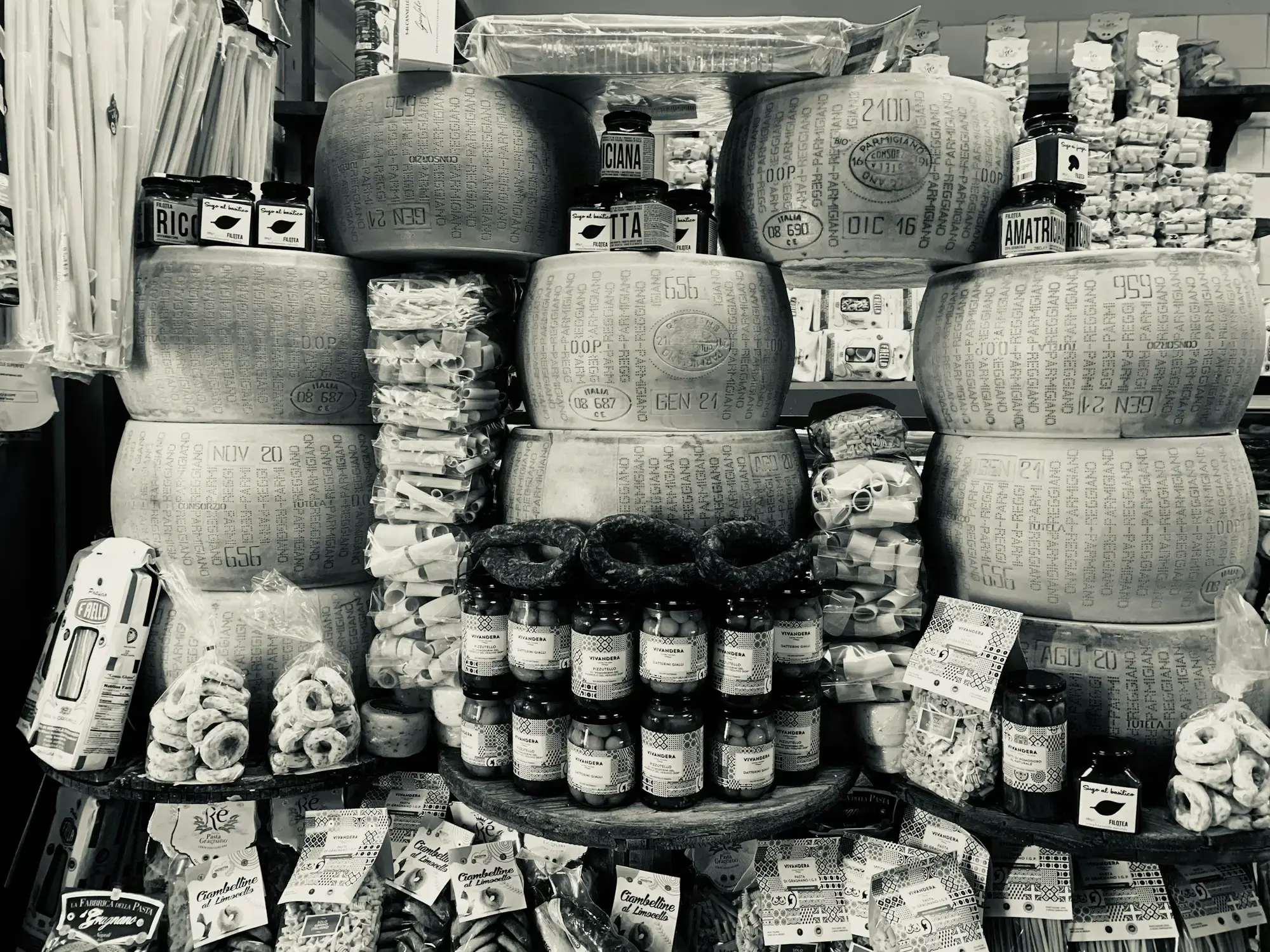 A display cabinet filled with whole cheese wheels and wedges in an Italian specialist food shop