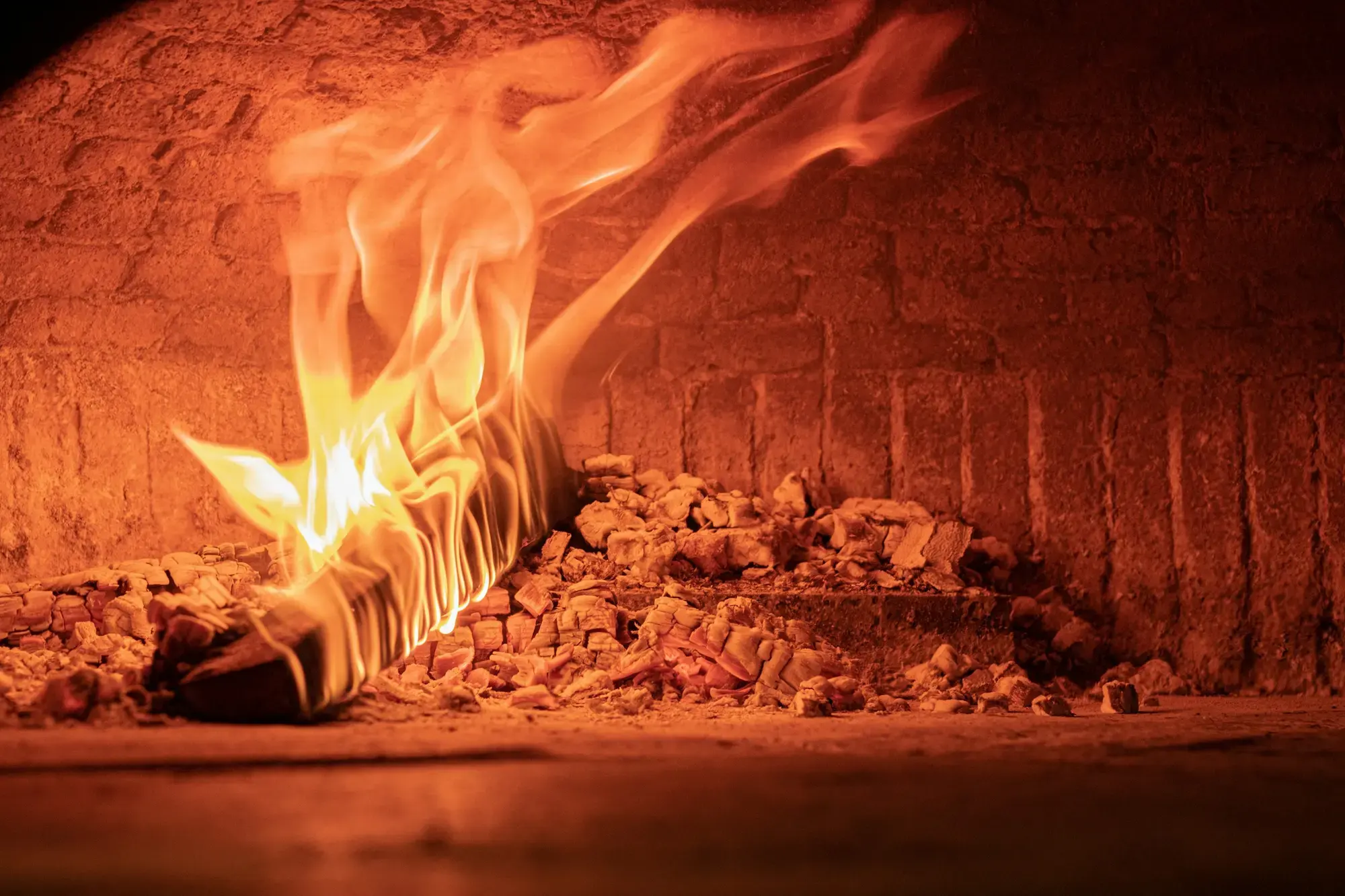 Flames rising from burning wood at the side of a domed brick pizza oven in Naples