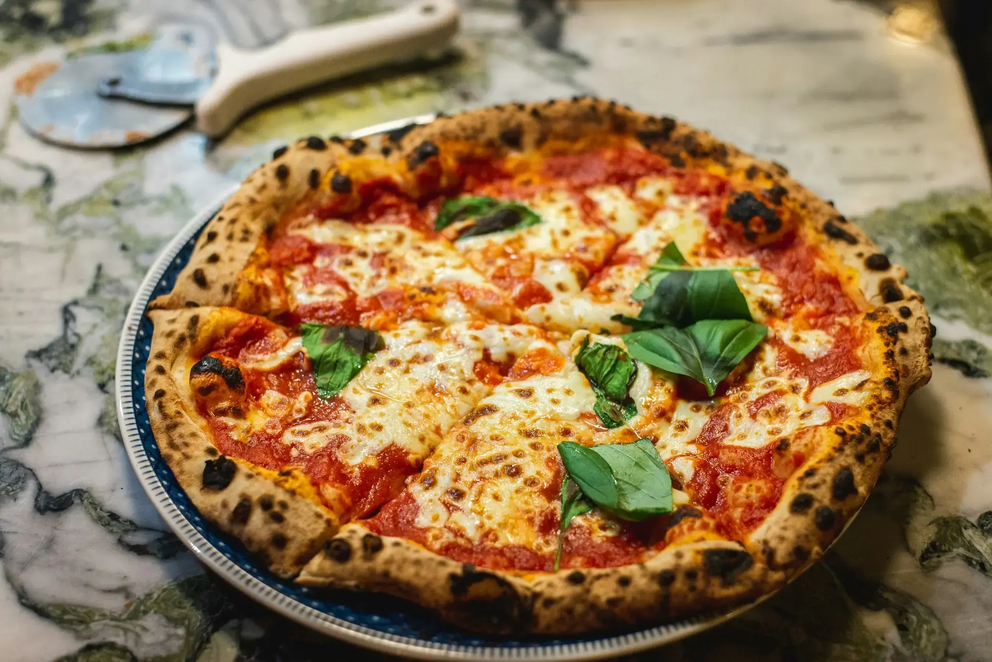 A Neapolitan-style pizza with a charred, puffy rim, cut into slices on a blue plate on a marble table in Paris