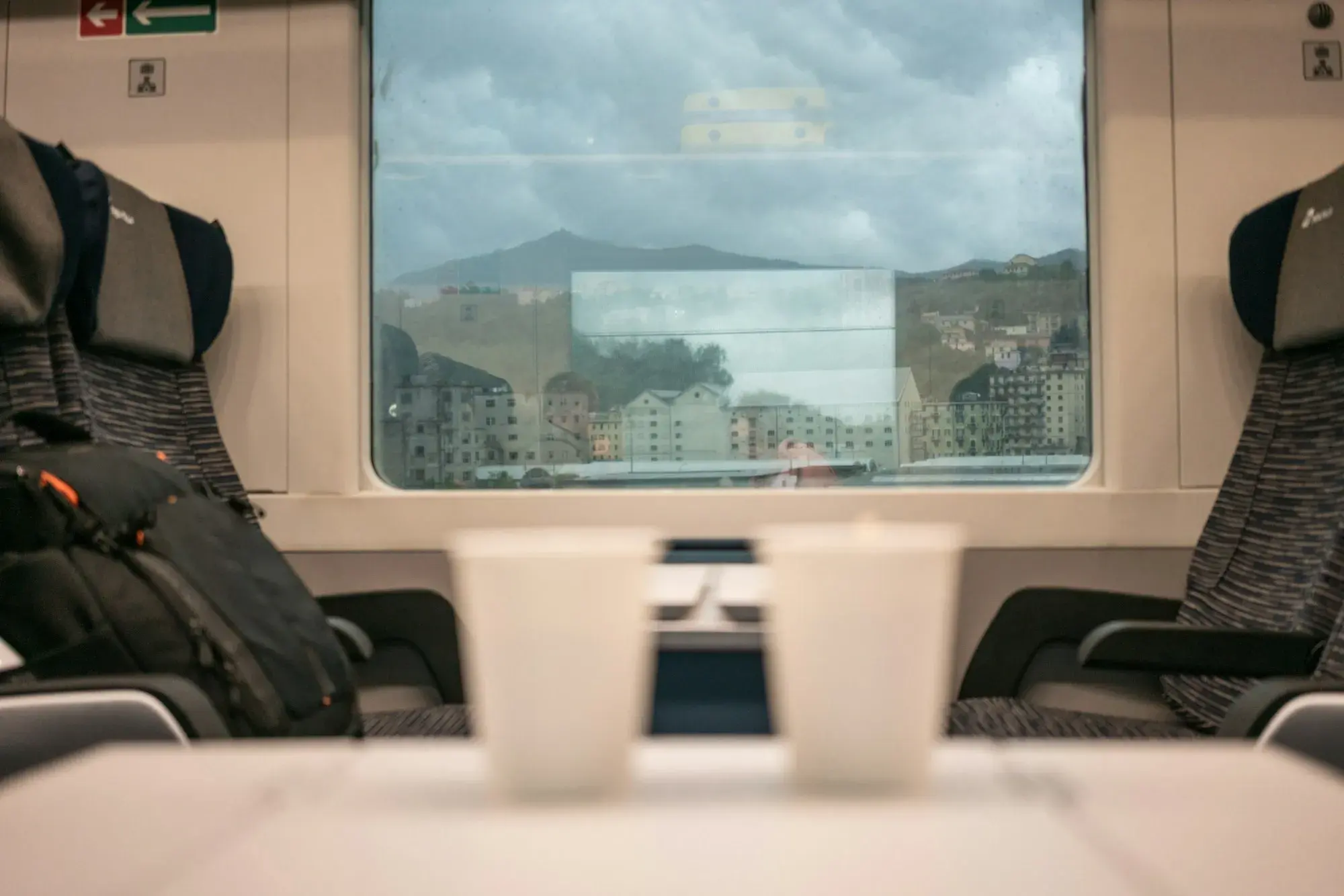 Inside a Trenitalia carriage, with seats around a table, two paper cups and a window onto the passing landscape